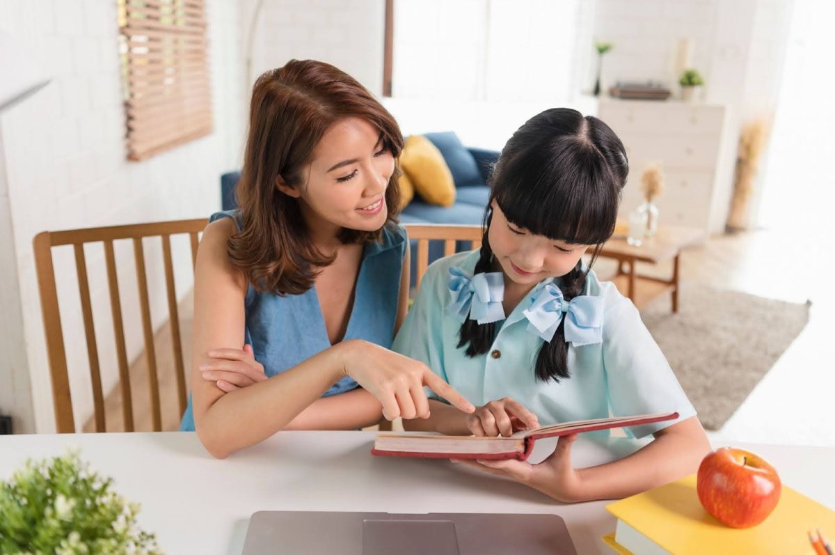 a smiling mother and her young daughter pointing at a book